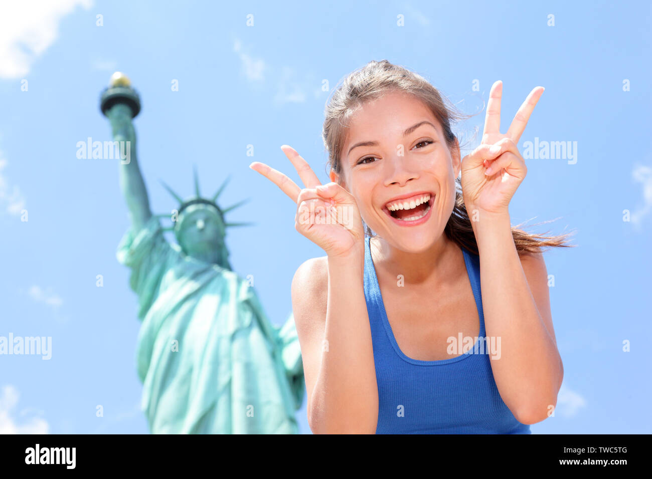 Turista en la Estatua de la Libertad, Nueva York, EE.UU. haciendo cara divertida expresión victoria mano signos entusiasmada y feliz. Concepto de turismo y viajes con gozosa de raza mixta mujer caucásica de Asia. Foto de stock