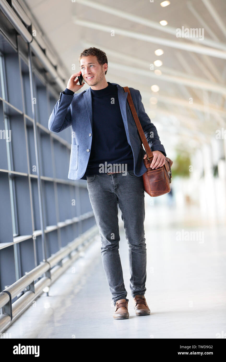 Hombre de negocios urbanos hablando por teléfono inteligente viajar  caminando en longitud de cuerpo completo dentro de aeropuerto. Joven  empresario casual vestidos de traje chaqueta y bolso. Guapo modelo  masculino en su
