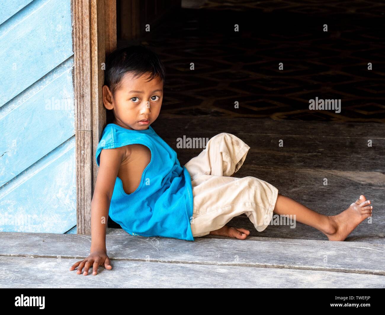 Chico sentado en la puerta delantera abierta, Sulawesi, Indonesia Foto de stock