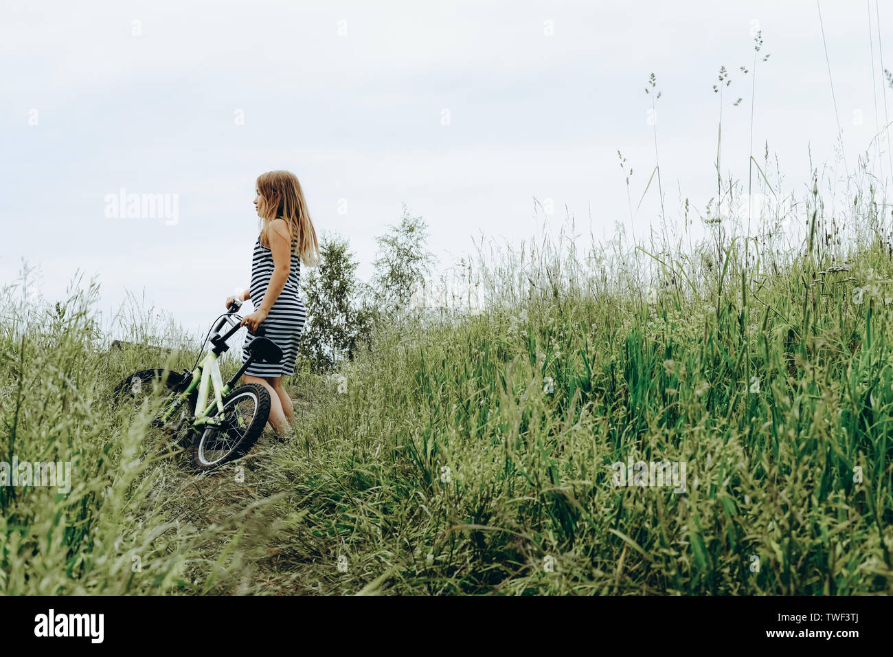 Chica en traje a rayas montando bicicleta. Pasar tiempo al aire libre. Niños jugando afuera en la primavera, el verano. Recuerdos de la infancia. Caminar en el parque, bosque. Ir de viaje, aventura en el desierto Foto de stock