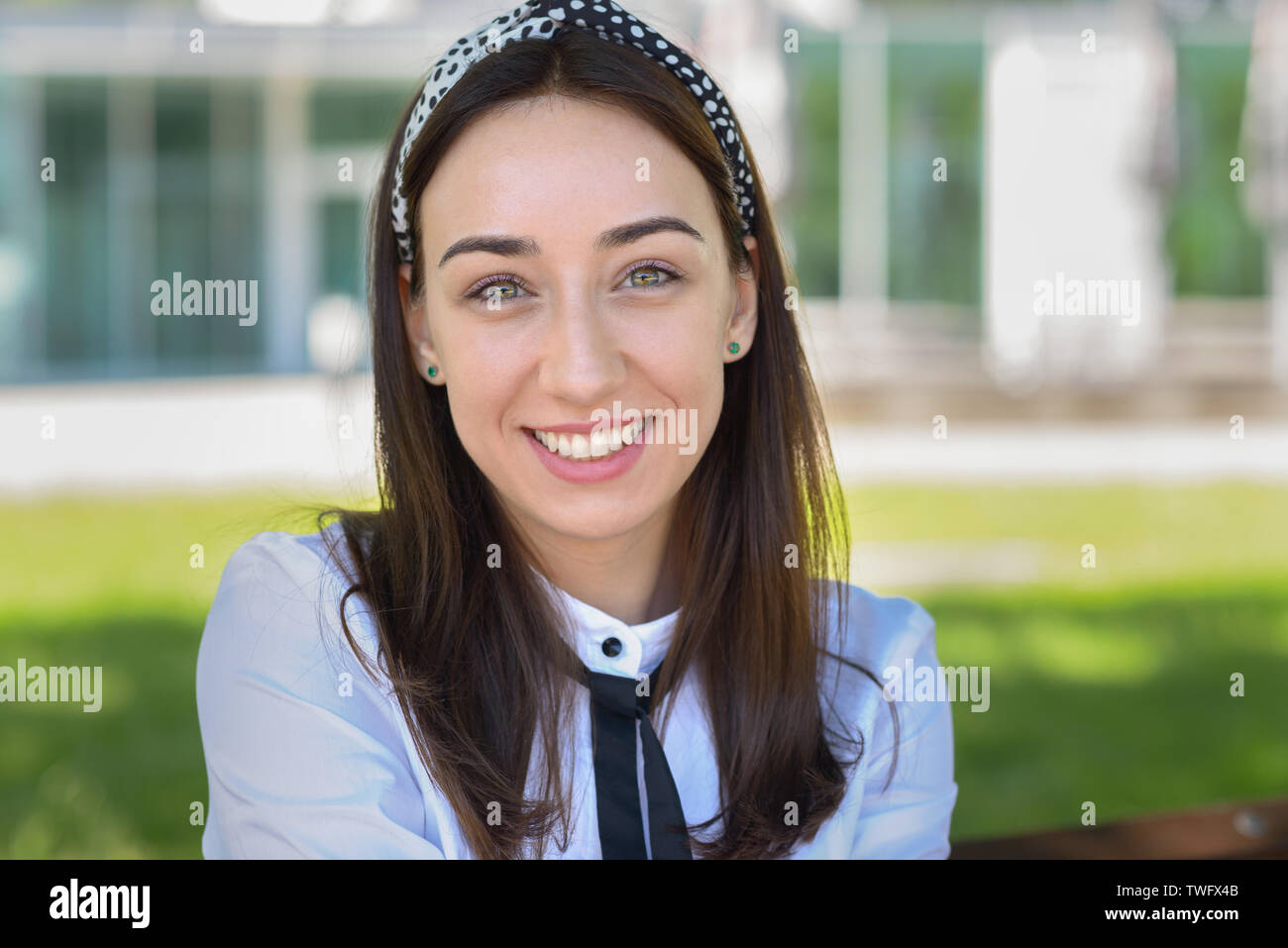 Amigable y atractiva mujer joven con una encantadora sonrisa posando al aire libre en un jardín a la sombra de un árbol Foto de stock