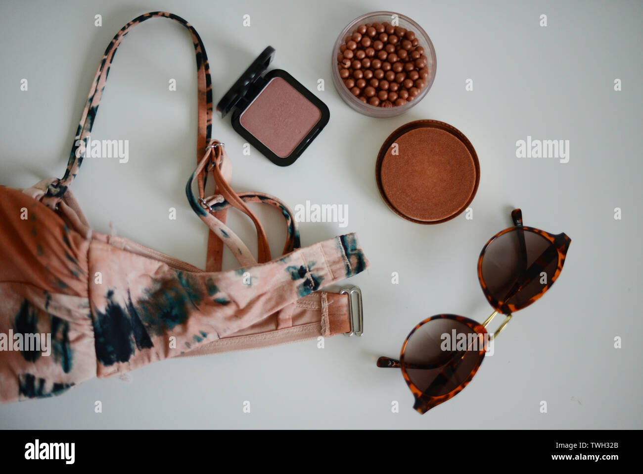 Bikini, sunglases y algunos productos de maquillaje en una tabla blanca Foto de stock