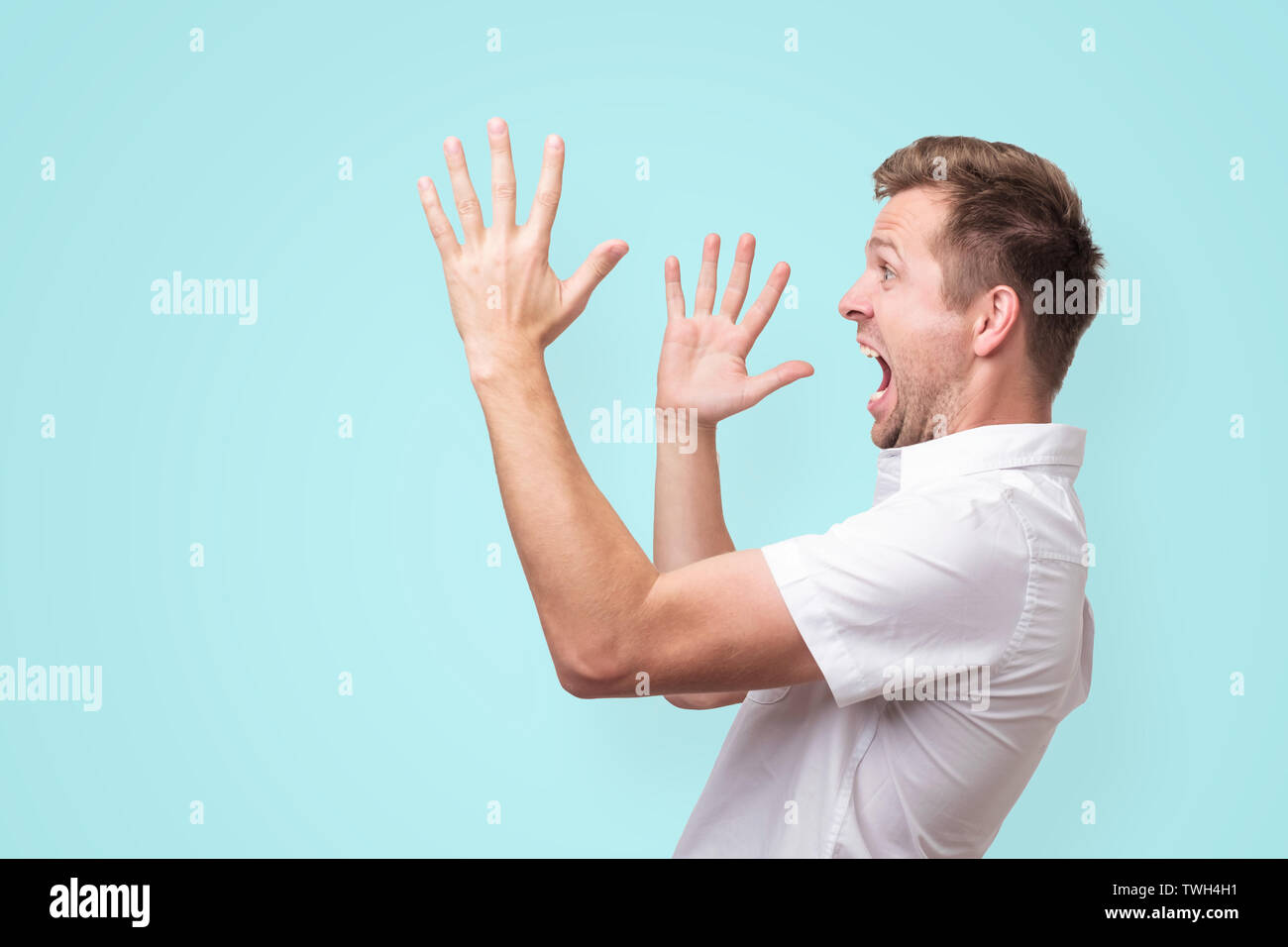 Joven gritando aparte con manos gesto aislado sobre fondo azul. Foto de stock