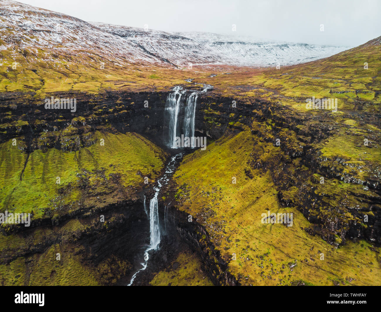 Imágenes aéreas de la Fosa de cascada desde arriba durante principios de la primavera con cumbres nevadas y verdes tonos (Islas Feroe, Dinamarca) Foto de stock