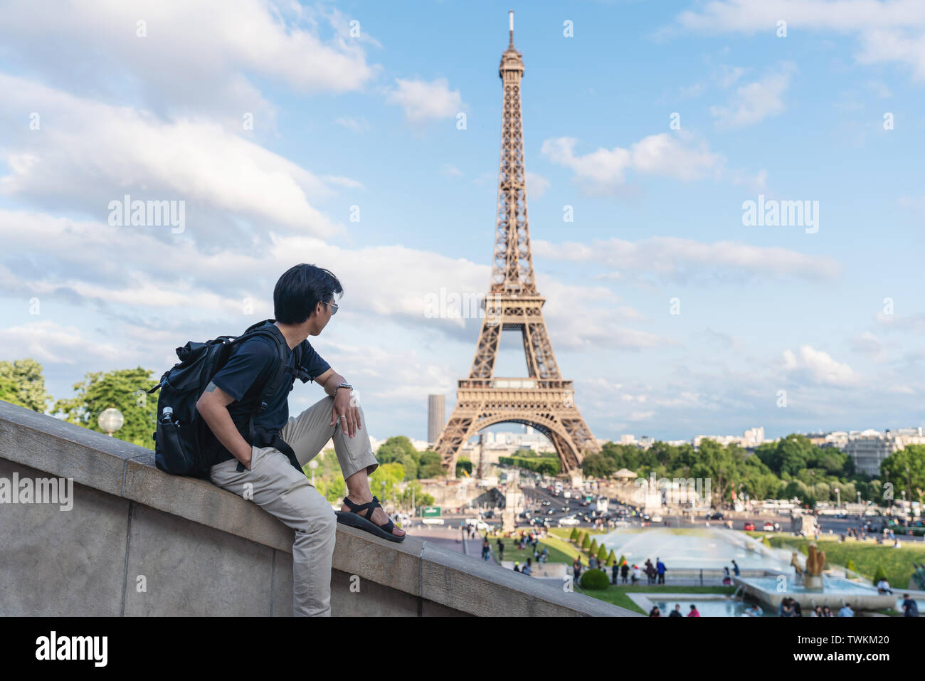 Un hombre con mochila mirando a la torre Eiffel, el famoso monumento y destino de viaje en París, Francia. Viajar por Europa en verano Foto de stock