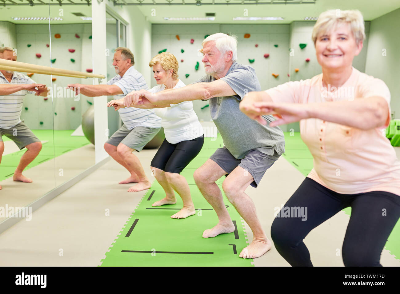 Grupo de ancianos vital hacer sentadillas juntos en la clase de fitness en el gimnasio. Foto de stock