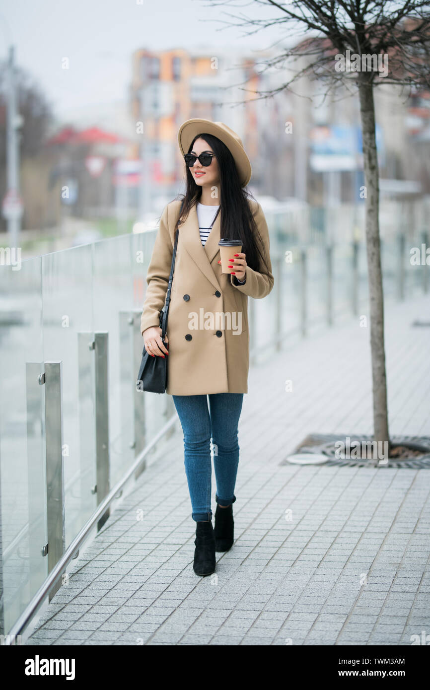 Mujer joven llevar abrigo y sombrero negro caminando en el otoño de las  calles de la ciudad y bebiendo café para llevar en vaso de papel. Desayuno  en el ir Fotografía de