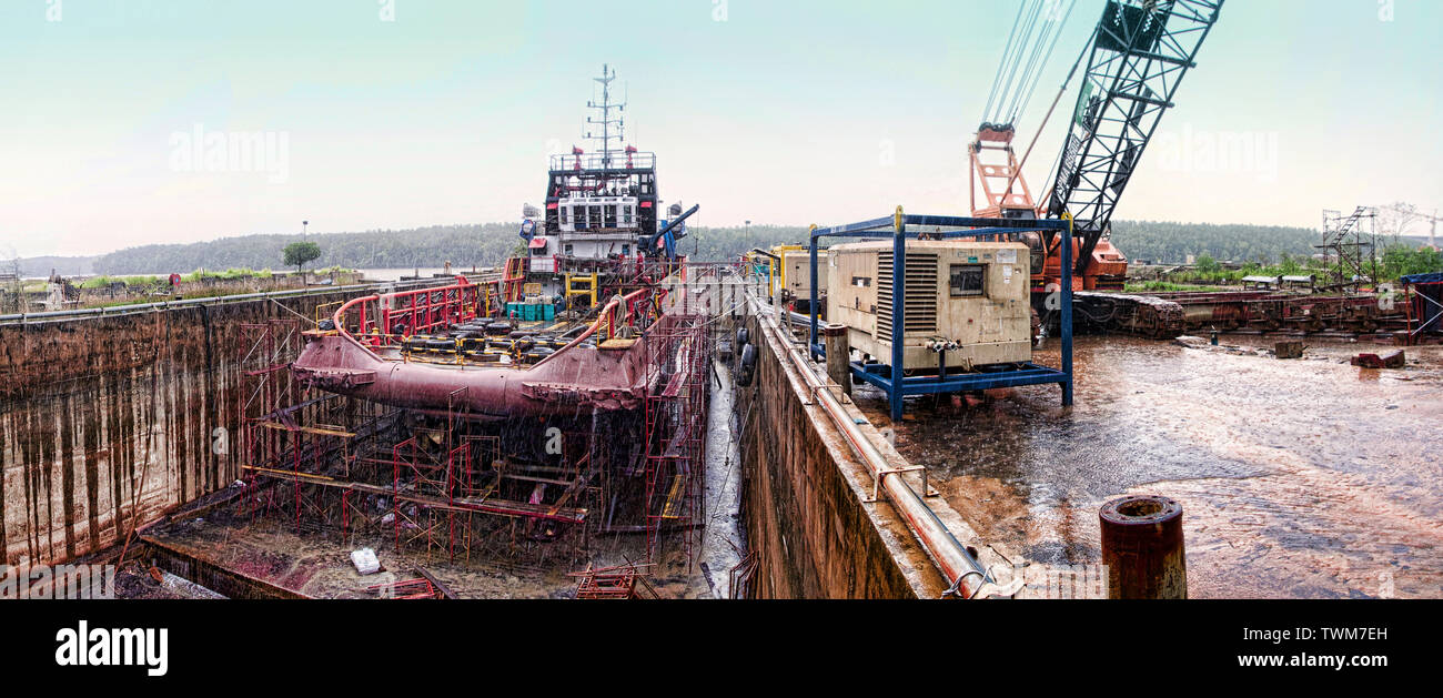 Buque de suministro offshore haciendo trabajo de mantenimiento en seco durante la lluvia de día acoplado Foto de stock