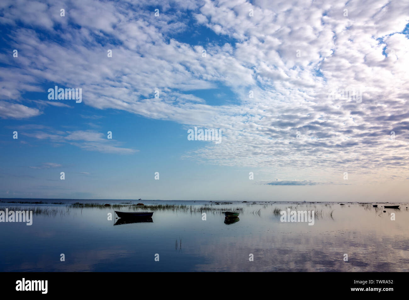 Pequeños barcos de pesca en el ancla, reflejadas en las tranquilas y claras aguas del lago, están cubiertos con juncia temprano en la mañana contra el hermoso amanecer de suaves tonos pastel. Foto de stock