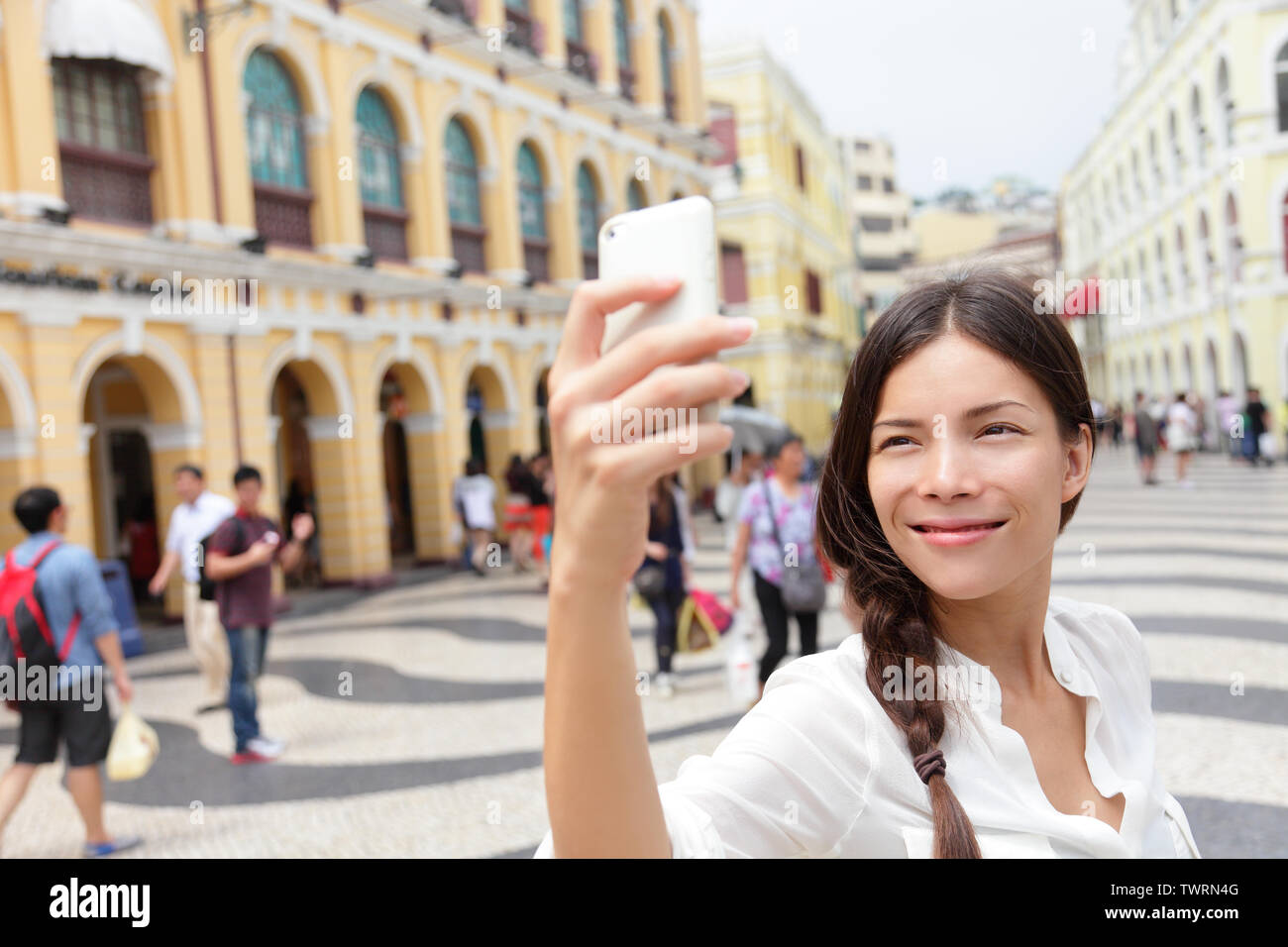 Mujer tomando fotografías selfie turístico en Macao, China, en la Plaza del Senado o la Plaza del Senado. Chica asiática turística teléfono inteligente con cámara para tomar fotografías mientras viajaba en Macao. Concepto de viajes y turismo. Foto de stock
