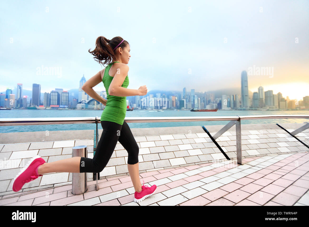 Ciudad corriendo - mujer runner y horizonte de Hong Kong. La atleta femenina atleta fitness entrenamiento de jogging viviendo un estilo de vida saludable en Tsim Sha Tsui, el paseo y la Avenida de las estrellas en el puerto de Victoria, Kowloon. Foto de stock