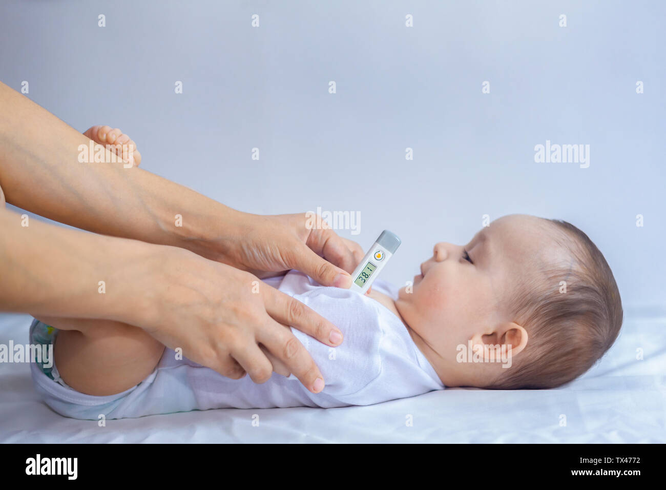 Joven mamá medición de temperatura del pequeño niño enfermo. Con termómetro  para tomar la temperatura del bebé en la axila. Un termómetro que muestra  un rango alto de kid's te Fotografía de