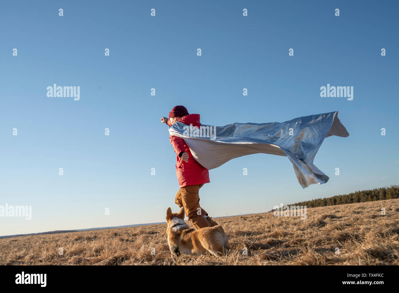 Chico vestido como superhéroe corriendo con el perro en el paisaje de estepa Foto de stock