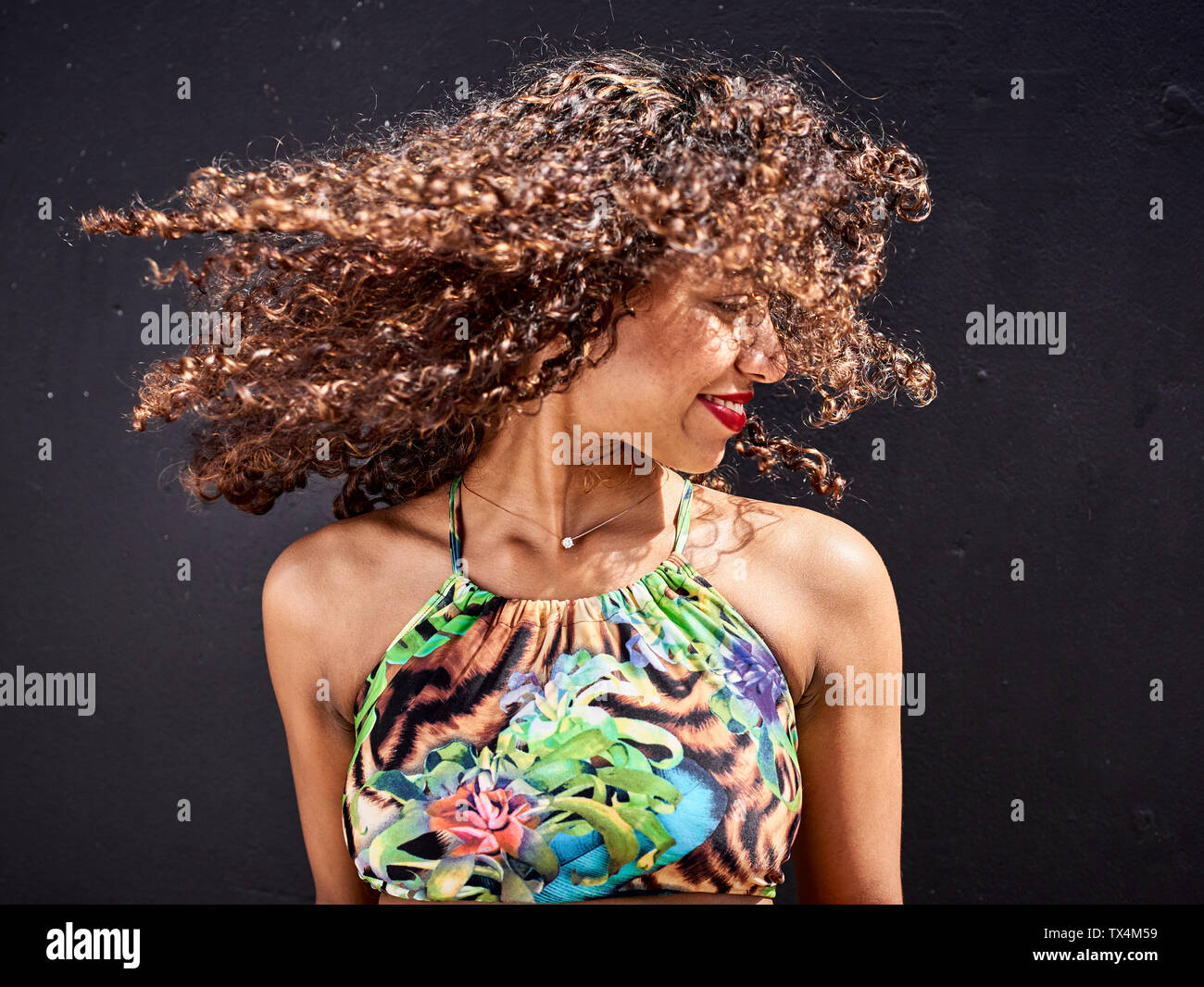 Mujer sonriente sacudiendo su pelo rizado delante de un fondo oscuro Foto de stock