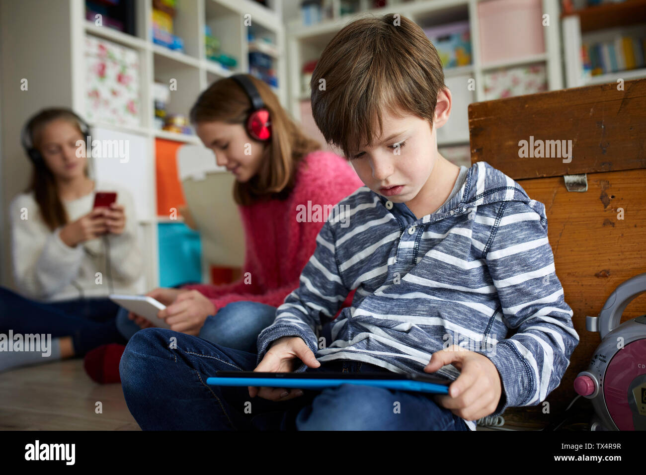 Hermanos jugando en casa con sus tabletas digitales, sentado en el suelo Foto de stock