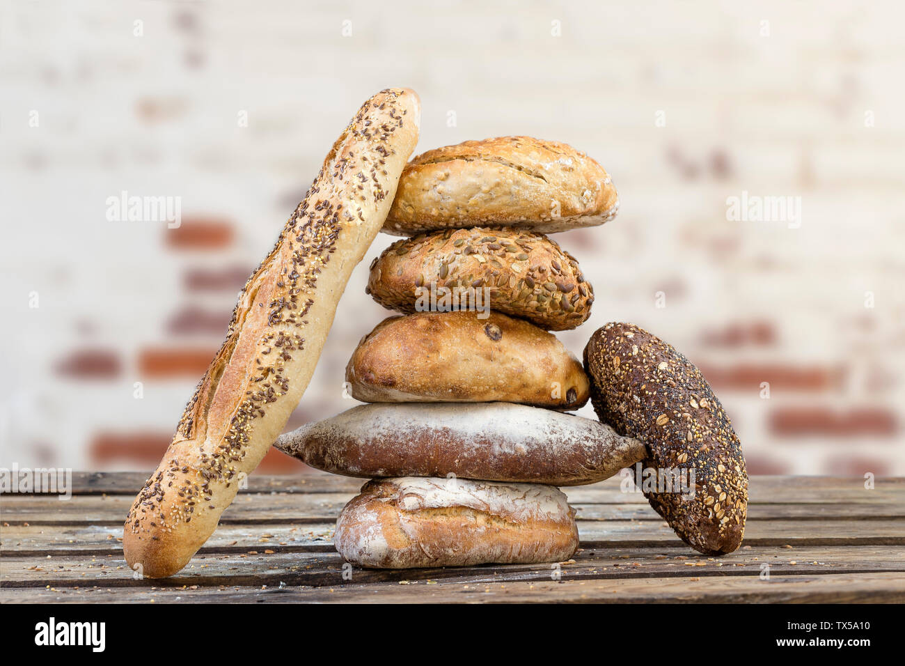 Montón de varios pequeños múltiples formas diferentes de grano y pan baguette,todo espolvoreado con semillas de girasol, lino y las semillas de sésamo y espigas de trigo y cebada más vieja pared de ladrillo rojo Foto de stock