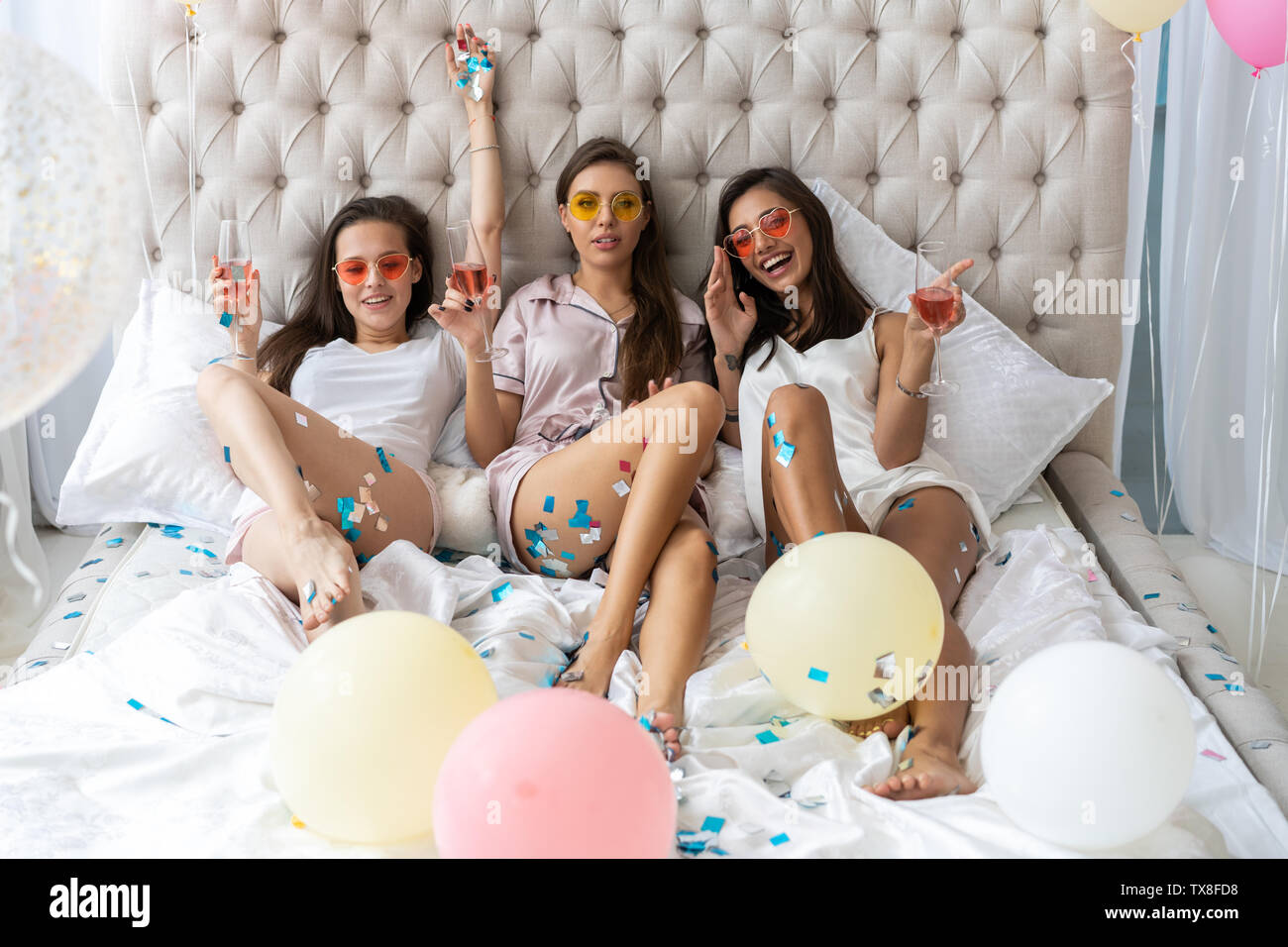 Pajama Party. Atractiva mujer joven sonriente en pijama bebiendo champán mientras tener una fiesta de pijamas en el dormitorio Foto de stock