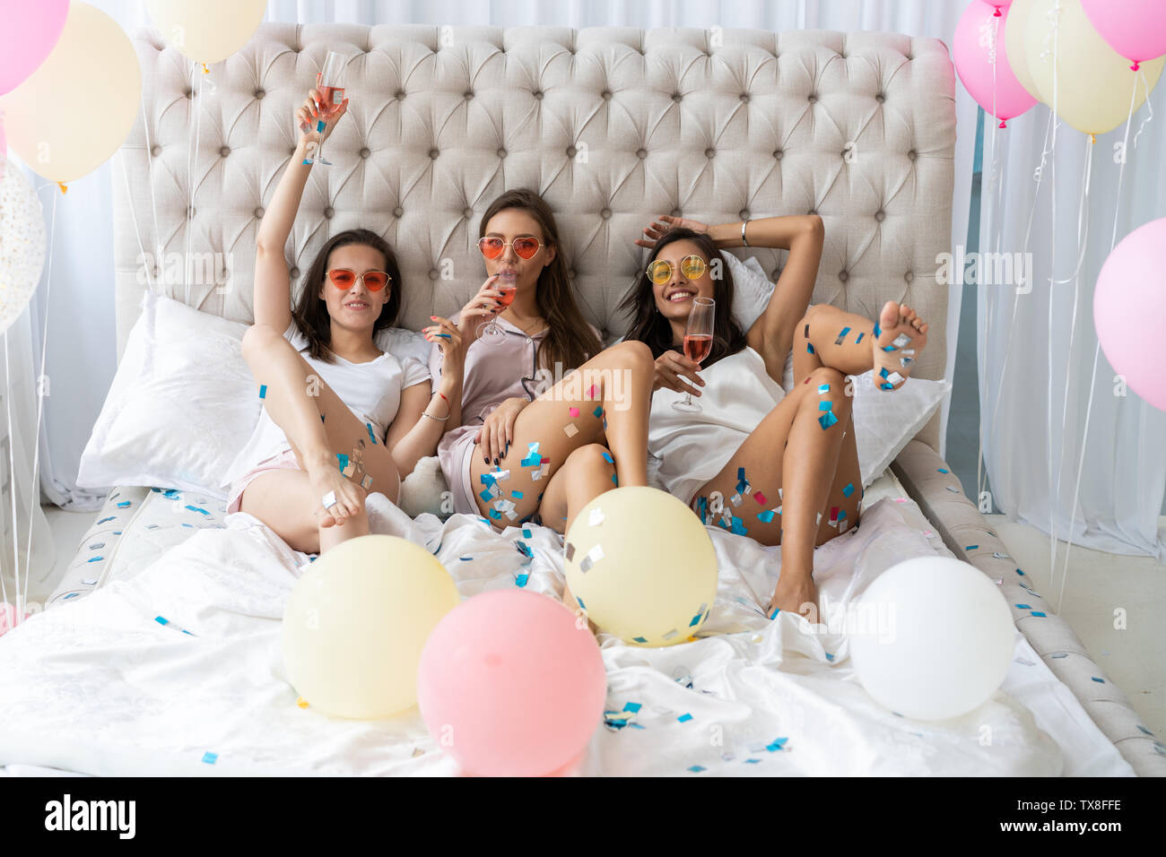 Pajama Party. Atractiva mujer joven sonriente en pijama bebiendo champán mientras tener una fiesta de pijamas en el dormitorio Foto de stock