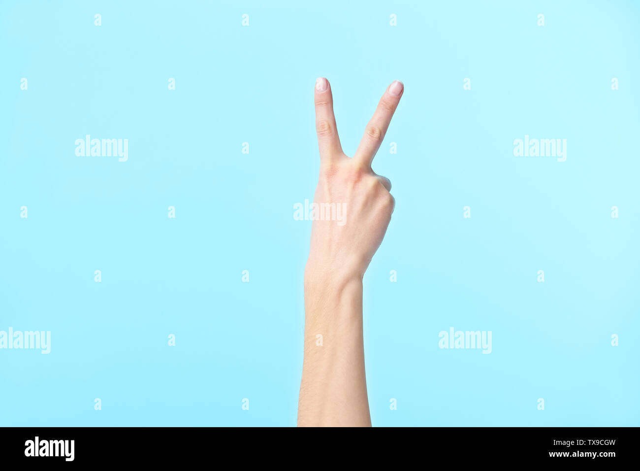 La mano humana mostrando el número dos, aislado sobre fondo azul. Foto de stock