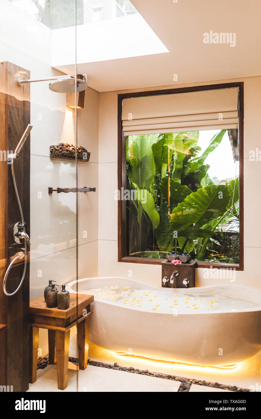 Interior moderno cuarto de baño con bañera y vistas al jardín tropical a  través de la ventana. Flor con espuma de baño de burbujas y flores  amarillas en spa Fotografía de stock -