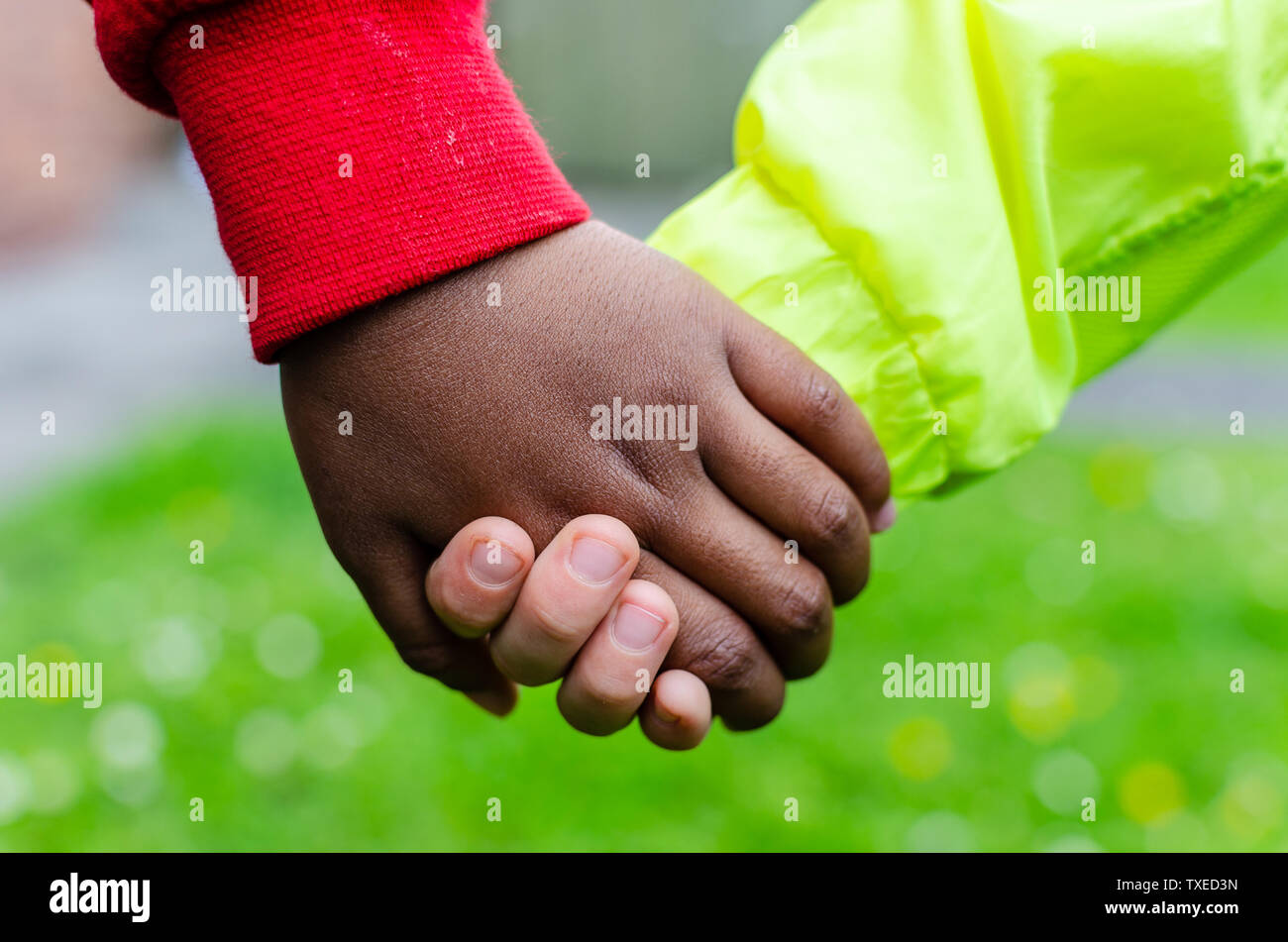 Dos niños de diferentes razas tomados de las manos juntas. La foto muestra la amistad, la igualdad y la diversidad. Uno caucásico el otro es oscuro (negro). Foto de stock