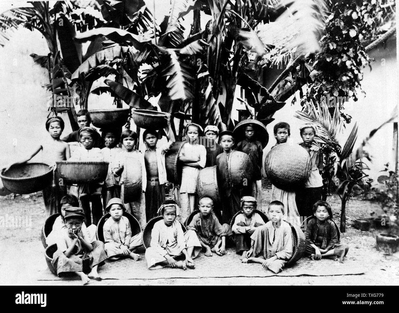Los niños con cestas fabricada localmente planteaban debajo de una palmera, Saigón, Vietnam del Sur en Saigón fue la capital y el centro comercial del colonialismo francés en Indochina Francesa Foto de stock