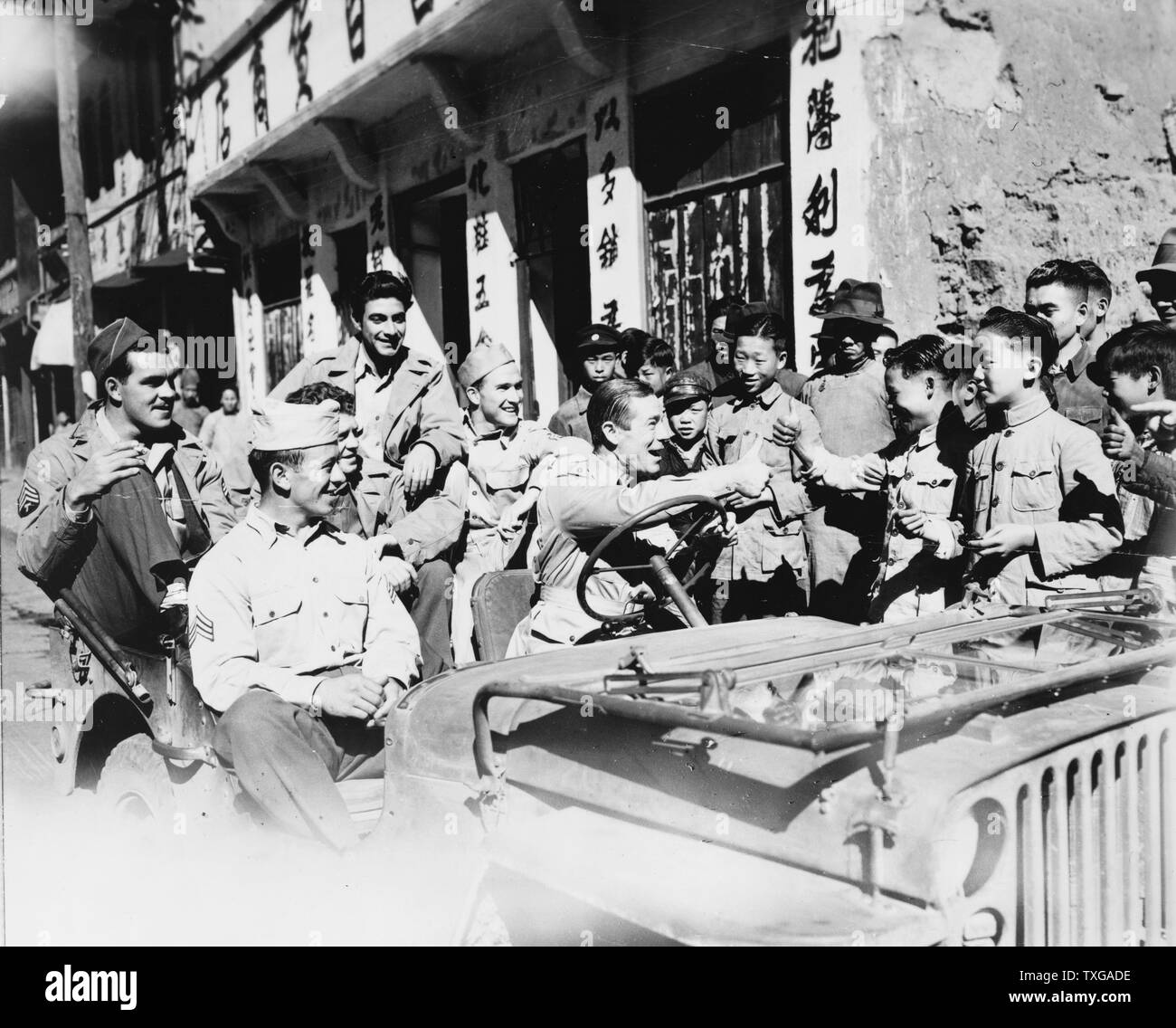 Joe E. Brown, el actor y comediante estadounidense jeep de conducción GLS, visitar los lugares de interés en China. Brown dando Thumbs up firmar a los niños chinos, 1942 o 1943. Foto de stock