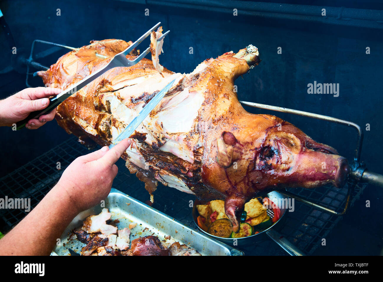 Chef cortando a mano cerdo entero a la parrilla para carnes con cuchillo.  Cerdo a la parrilla tradicional carbón y fuego. El pequeño cerdo es asado  entero en un fuego abierto. P