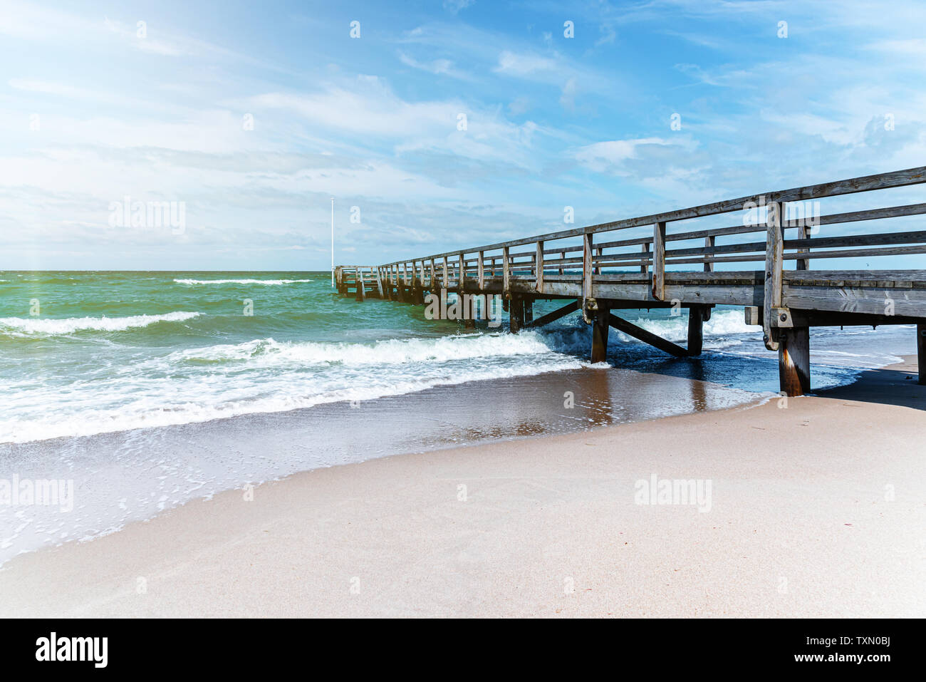 Muelle de madera sobre la arena de la playa contra el mar y el cielo azul del verano en día soleado Foto de stock