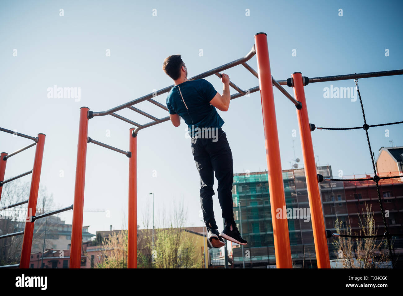 Calistenia en el gimnasio exterior, joven haciendo tirar ups en equipos de ejercicios, vista trasera Foto de stock