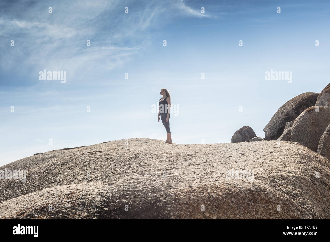 Mujer joven practicando yoga tomando un descanso mirando desde la playa de Boulder, Ciudad del Cabo, Western Cape, Sudáfrica Foto de stock