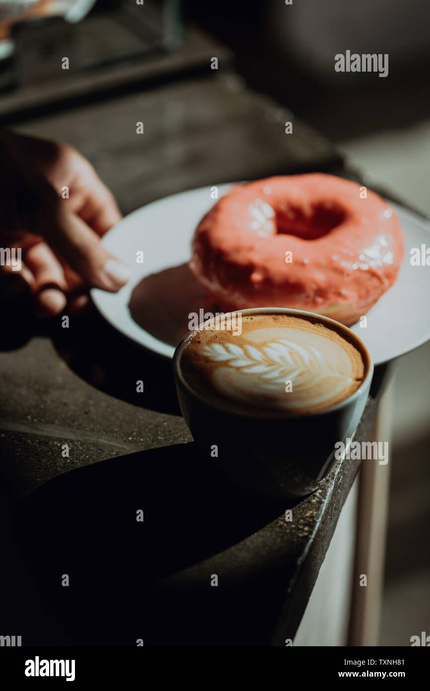 Barista colocando el anillo donut por taza de café en la cafetería, contador de clave baja enfoque superficial Foto de stock