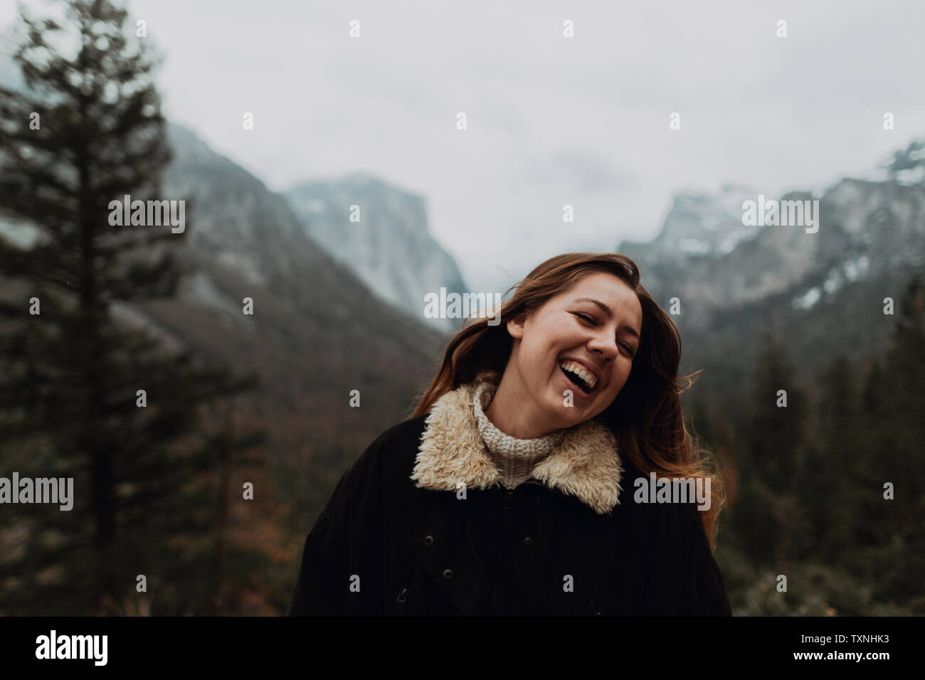 Mujer joven riendo en paisajes de montaña, la cabeza y los hombros, Yosemite Village, California, EE.UU. Foto de stock
