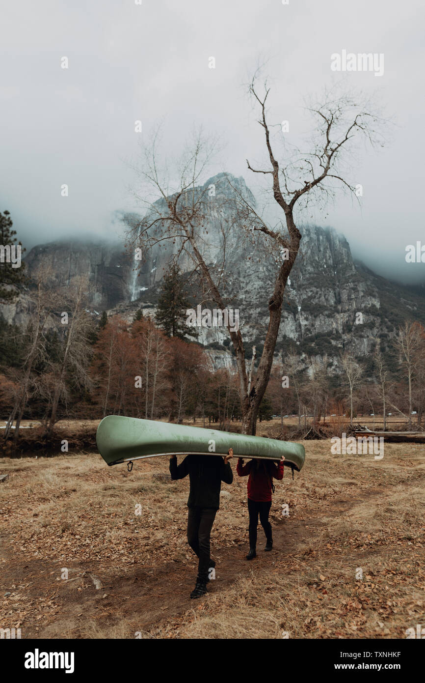 Los jóvenes piragüismo par llevar canoa sobre cabezas en paisajes de montaña, Yosemite Village, California, EE.UU. Foto de stock