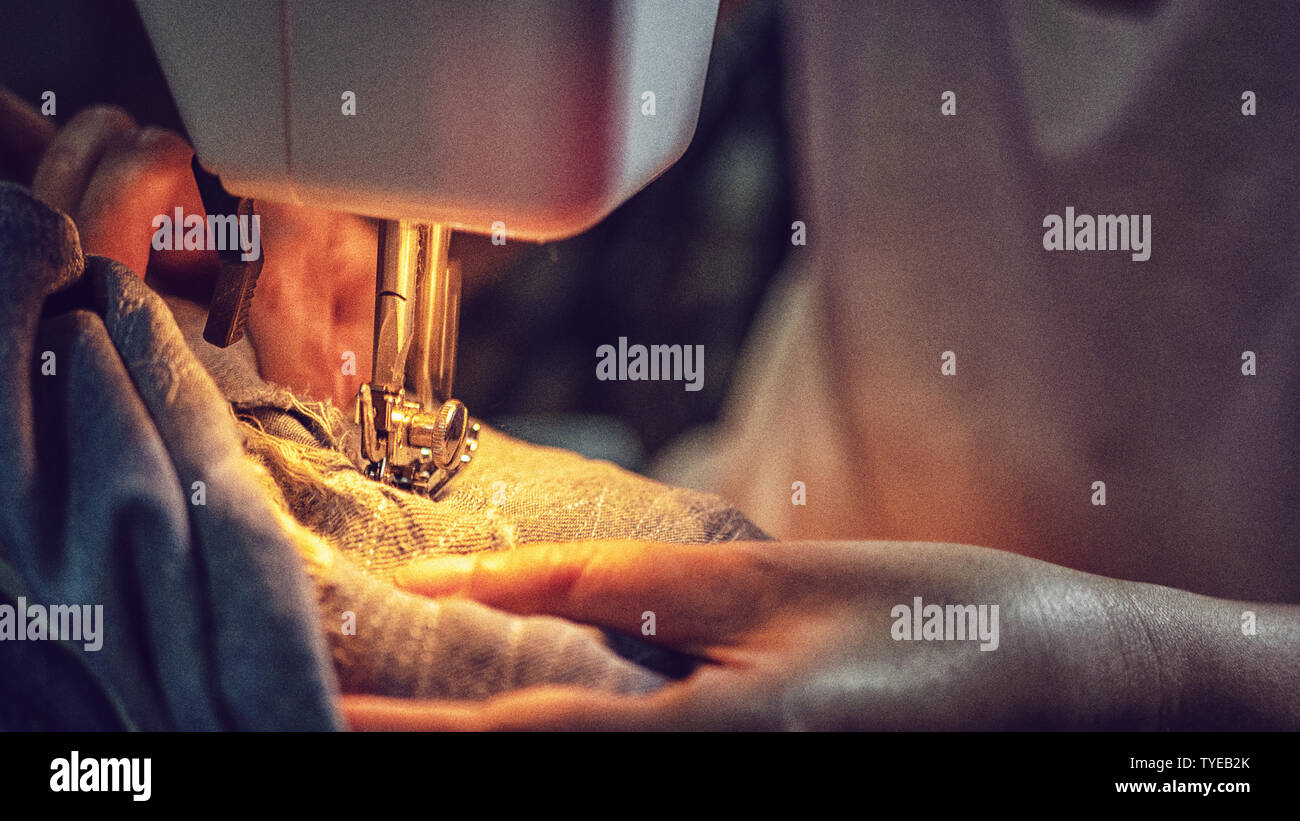 Primer plano de una mujer cosiendo pantalones vaqueros azules con una máquina de coser Foto de stock