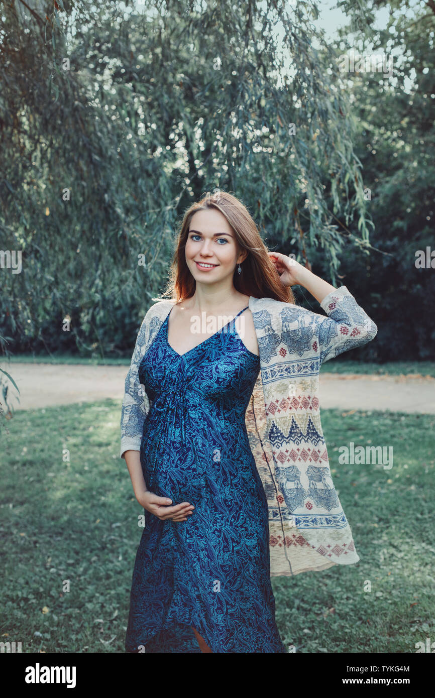 Feliz saludables durante el embarazo y la maternidad. Retrato de caucásica joven embarazada vestidos de largo vestido azul posando en el parque afuera. Hermosa e femenino Fotografía de stock - Alamy