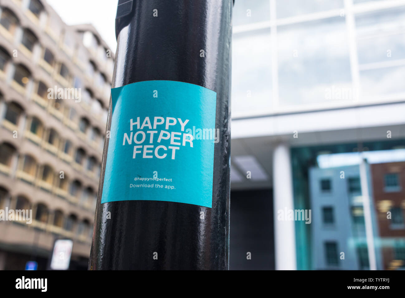 Pegatina con palabras feliz no es perfecto, una nueva meditación y Mindfulness app, sobre un poste de la luz en Londres Foto de stock