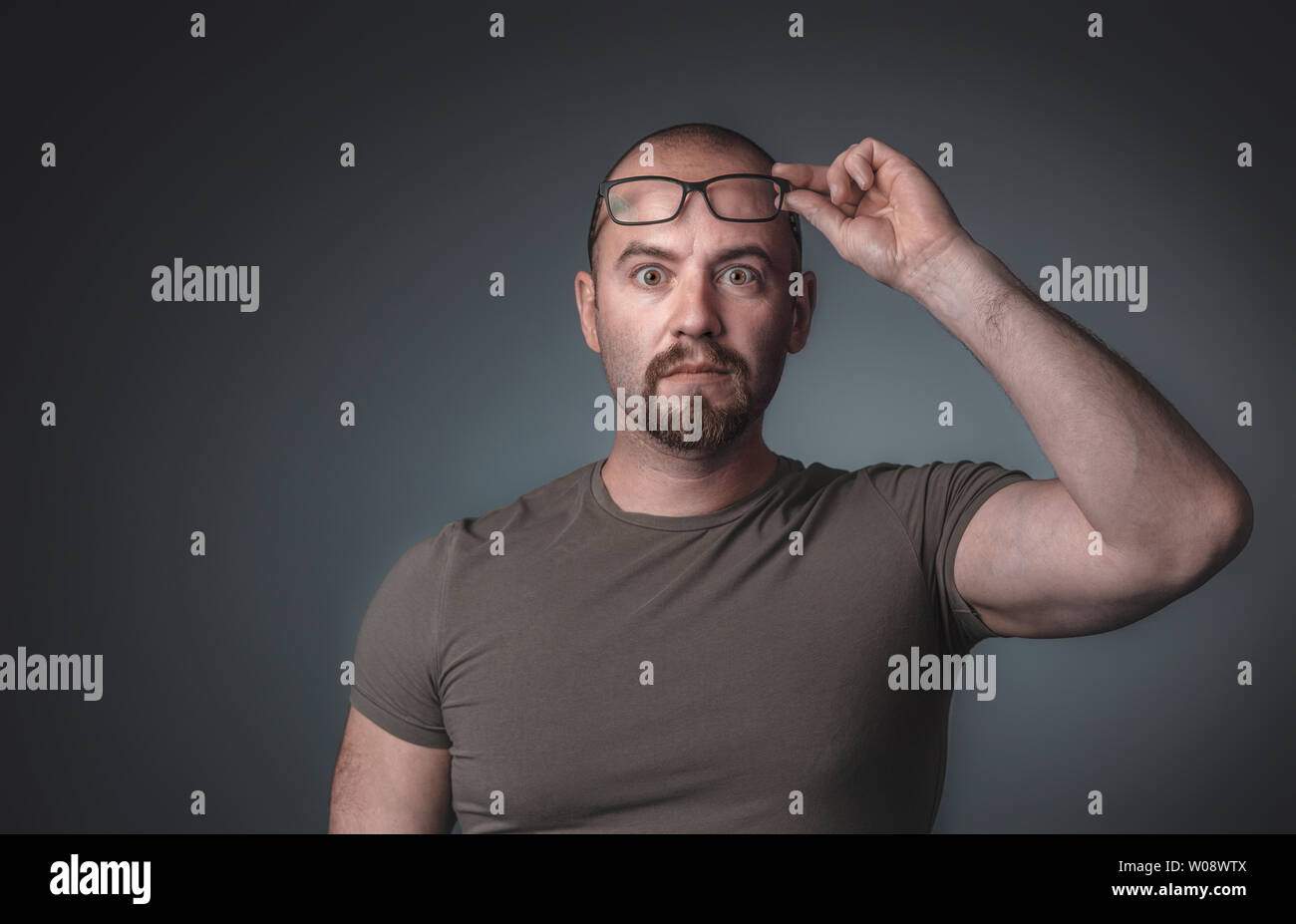 Retrato de un hombre con expresión sorprendida que levanta sus gafas, viste una camiseta, toma en el estudio. Foto de stock
