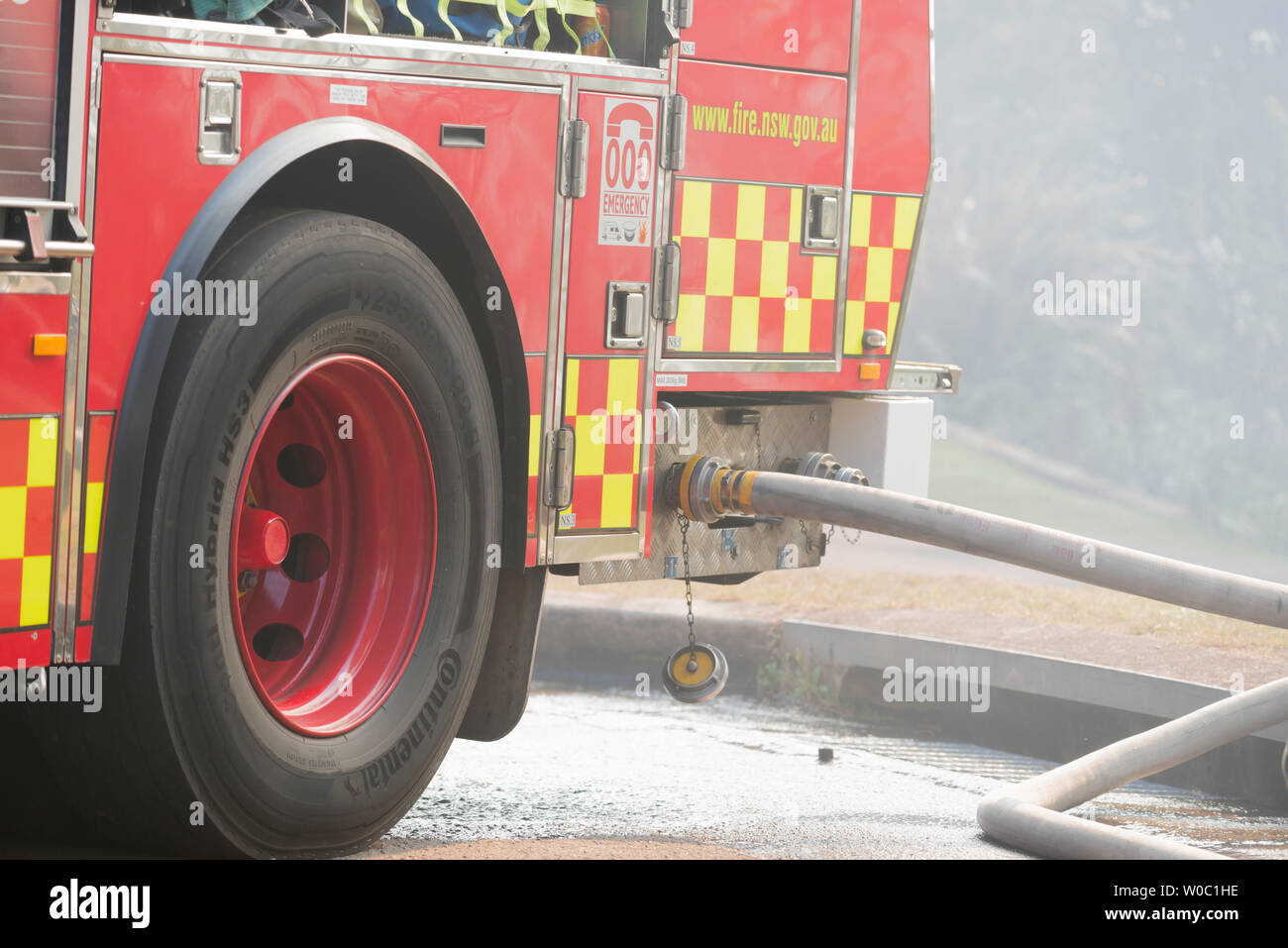 Un incendio de Nueva Gales del Sur y el camión de rescate con mangueras contra incendios conectado, estacionado en una calle llena de humo suburbano durante una reducción del peligro de quemadura en Sydney Foto de stock