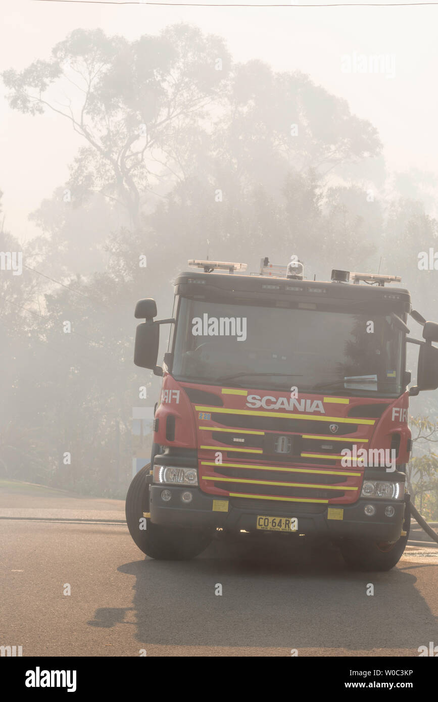Un incendio de Nueva Gales del Sur y el camión de rescate con mangueras contra incendios conectado, estacionado en una calle llena de humo suburbano durante una reducción del peligro de quemadura en Sydney Foto de stock