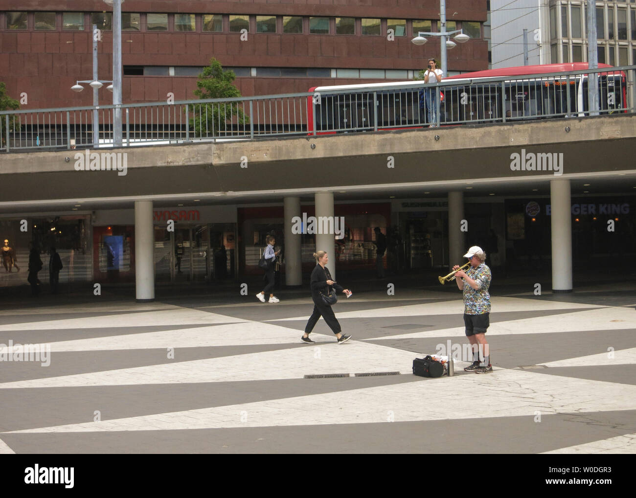 Un hombre solitario en pantalones cortos y tapón reproduce con una trompeta en Sergels torg en Estocolmo, Suecia Foto de stock