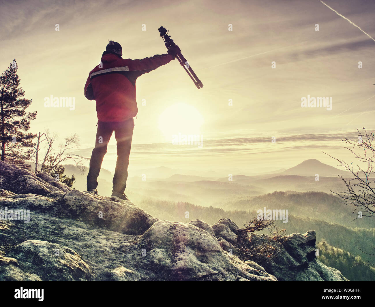 Fotógrafo con trípode en la mano. El hombre sostenga el trípode, de pie sobre una roca. Excursionistas admirando la impresionante cordillera brumosas mañanas soleadas. En un viaje épico wi Foto de stock