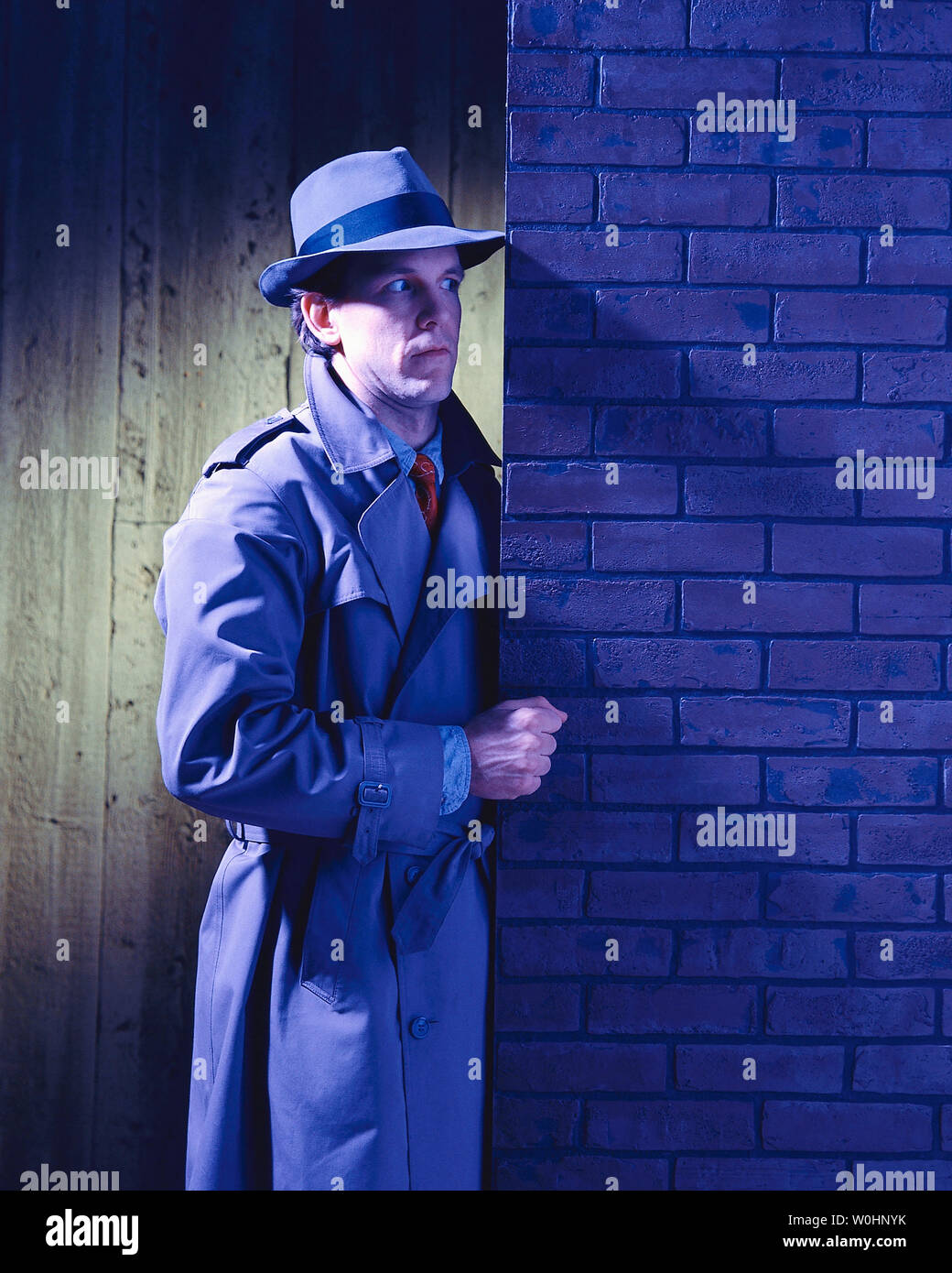 Hombre de pie fuera en la noche, con sombrero y trinchera tratando de resolver un misterio Foto de stock