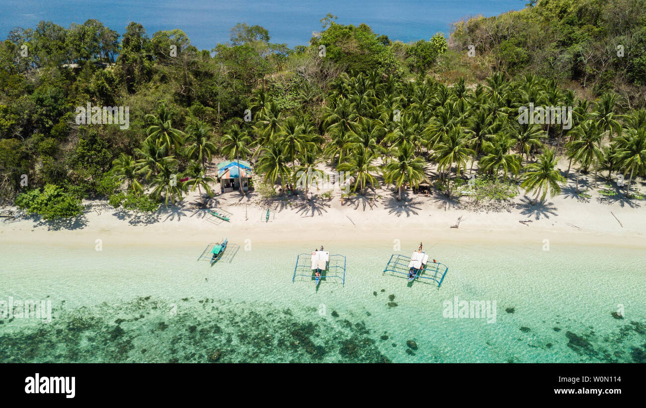 Botes filipinos tradicional situado en una playa tropical con palmeras y arenas blancas en un día soleado. Destino de viaje en Filipinas Foto de stock