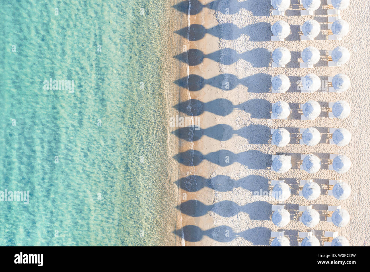 Vista desde arriba, la impresionante vista aérea de una increíble playa blanca vacía con sombrillas de playa blanca y aguas turquesas durante la puesta de sol. Foto de stock