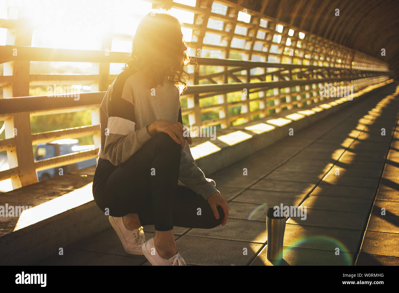 Esbelta joven morenita mujer bailarina callejera gimnasta sentarse y descansar con termo taza en la calle puente al amanecer Foto de stock
