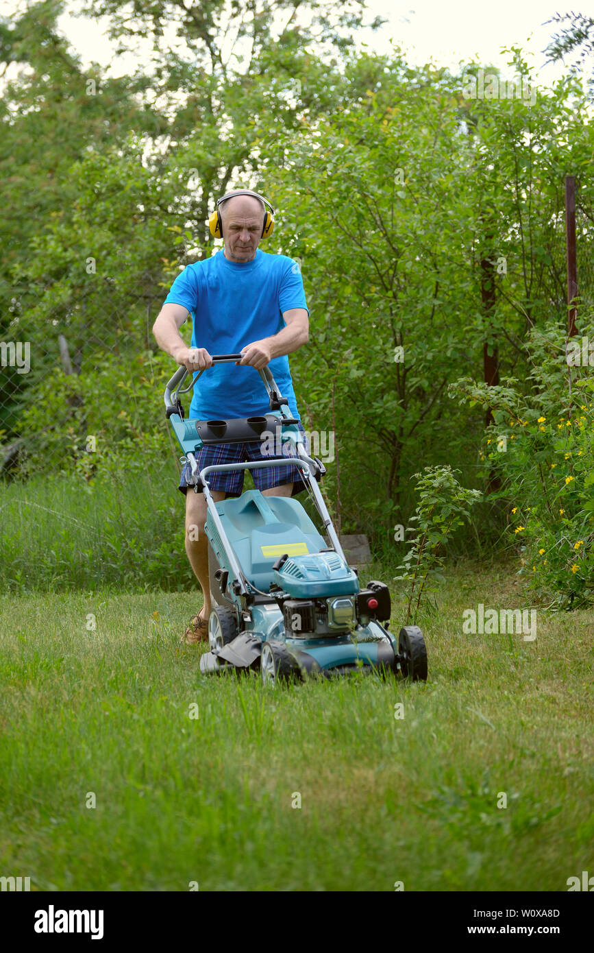 El hombre con auriculares siega un césped con la segadora de césped de  gasolina en el cálido verano Fotografía de stock - Alamy