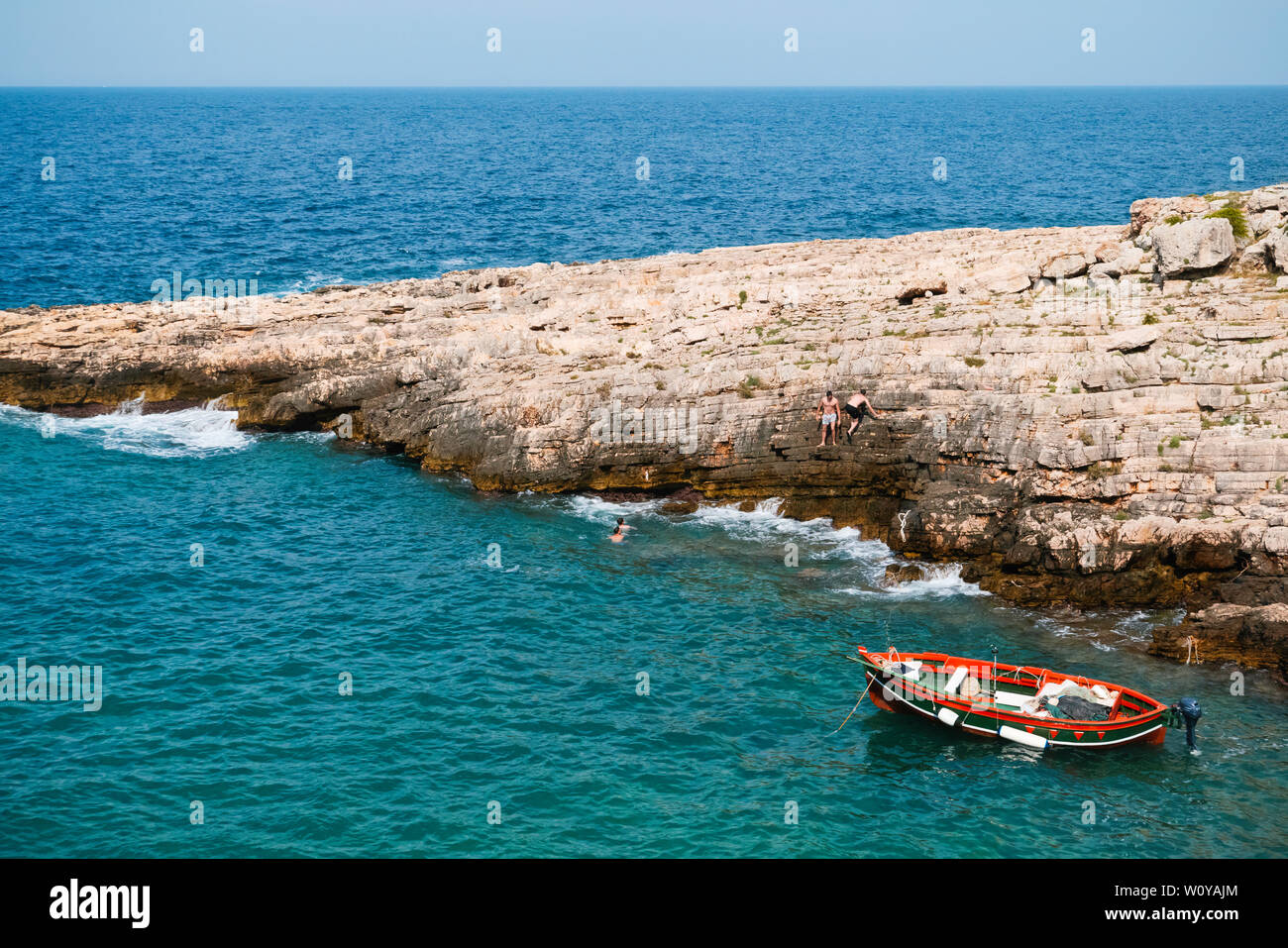 Barco amarrado y chicos irreconocible en verano caluroso atardecer en la playa rocosa del mar Adriático en Puglia . Foto de stock