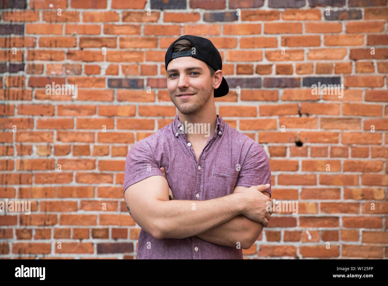 Apuesto joven hombre caucásico con sombrero hacia atrás para retratos  sonrientes delante del muro exterior de ladrillo texturado Fotografía de  stock - Alamy