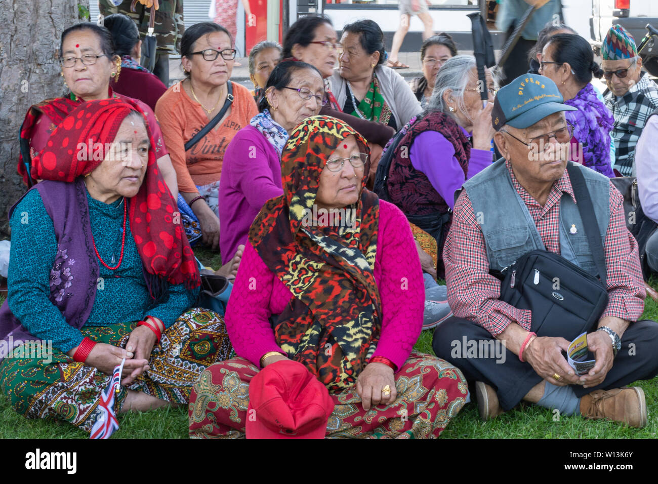 Comunidad nepalesa mayores sentados a la sombra en un día de las Fuerzas Armadas evento en Aldershot, Hampshire, Reino Unido, junio de 2019 Foto de stock
